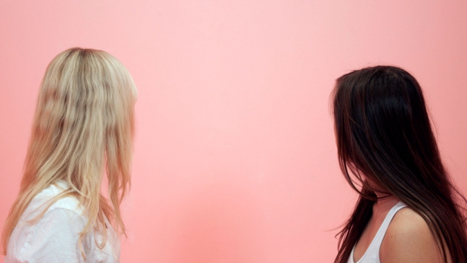 two people with long hair turned towards a pink wall